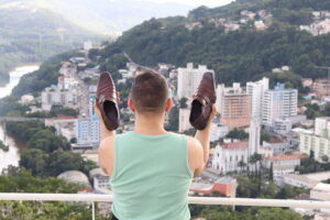 foto de elton kruger. na imagem joão tomaz carrega 2 sapatos olhando para a vista de Joaçaba
